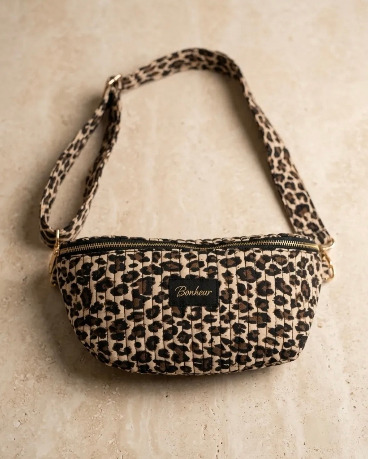 Sac banane matelassée léopard avec bandoulière réglable et zip, petite pochette chic. Bonheur affiché sur un badge.