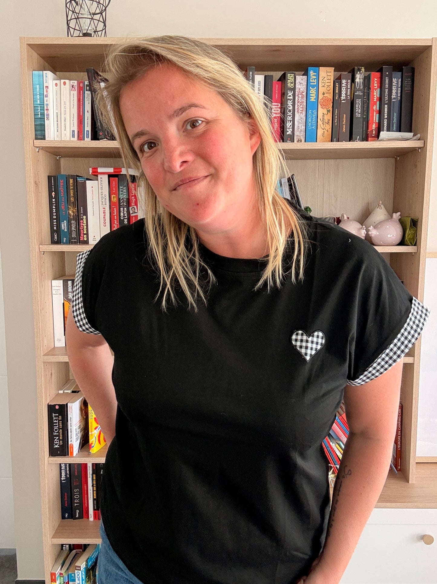 T-shirt femme noir oversize avec détails vichy noir et blanc, femme portant le vêtement près d’une étagère de livres.