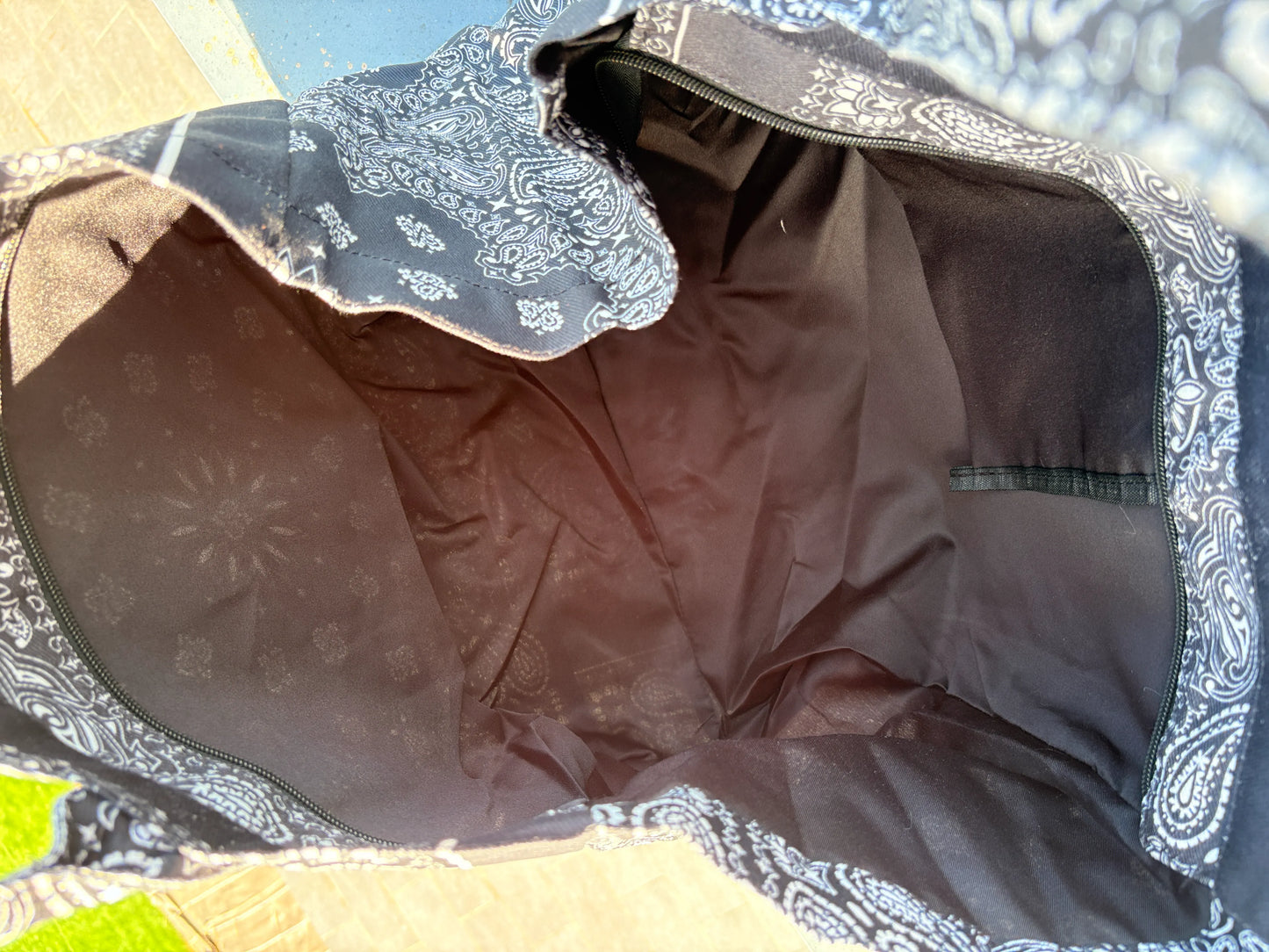Grand sac polochon noir à motif paisley, ouverture zippée montrant l’intérieur brun avec poche rectangulaire.
