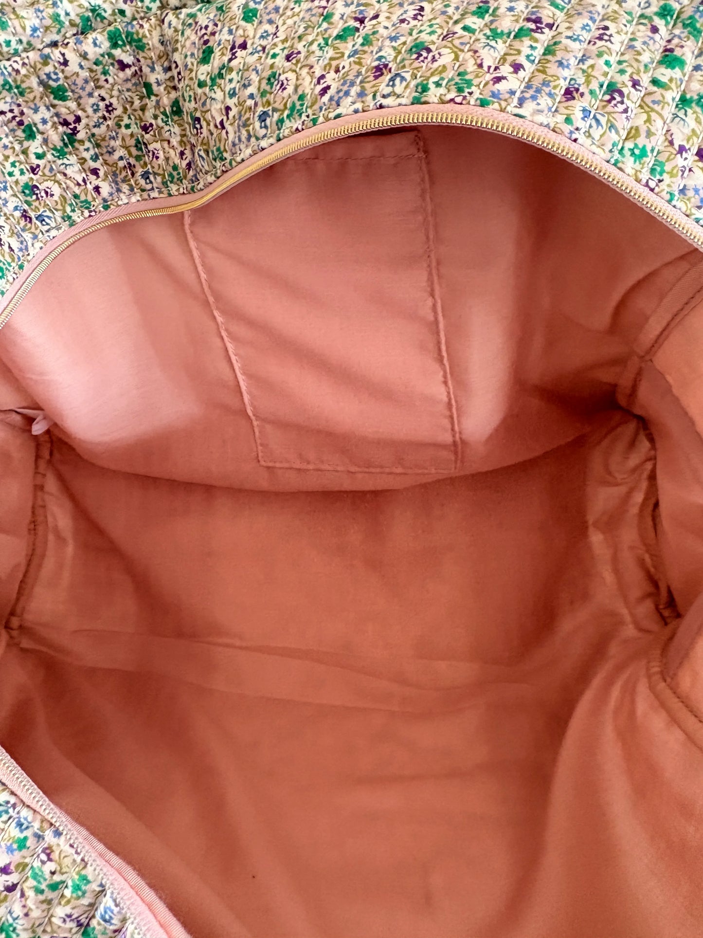 Sac polochon vert à motif floral, vue de l’intérieur montrant un tissu rose pâle, compartiments et doublure matelassée.
