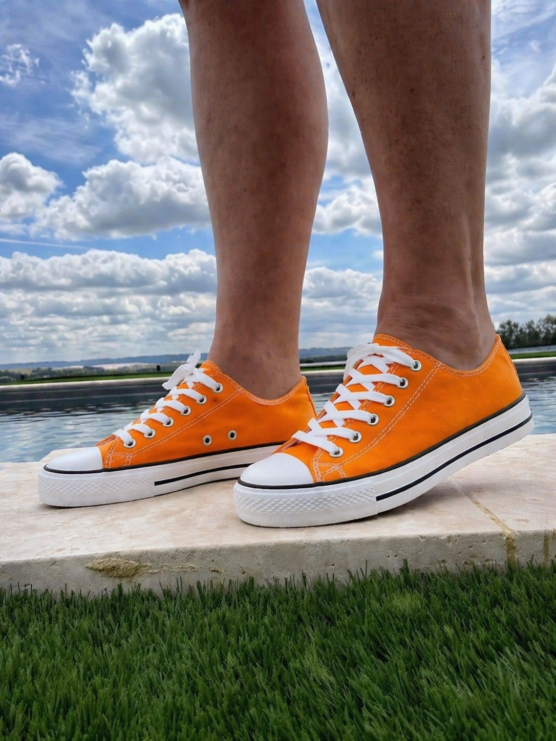 Baskets basses orange style Converse, vues au niveau des pieds sur terrain en extérieur près de l’eau.