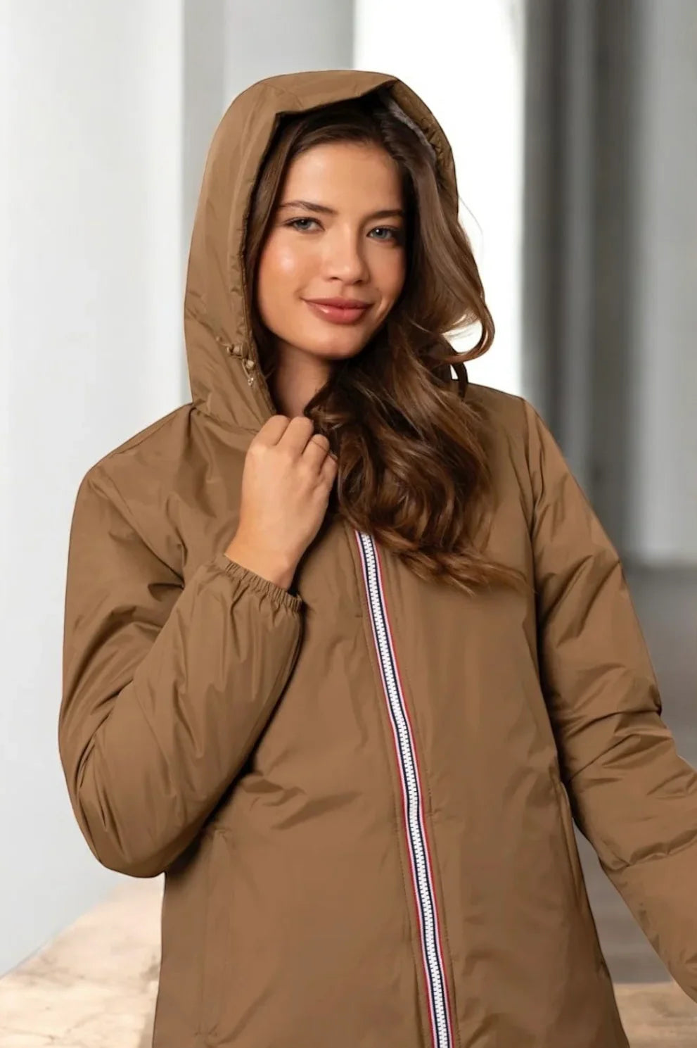 Femme portant une parka longue imperméable camel Laura Jo avec capuche ajustable et fermeture zippée tricolore