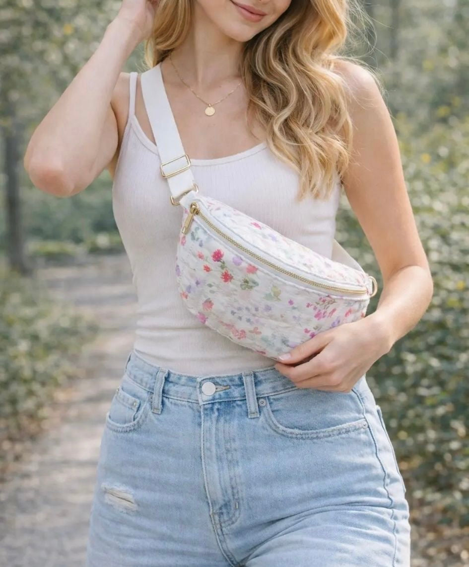 Sac banane blanc fleuri rose en tissu matelassé avec zip doré, porté en bandoulière par une femme.