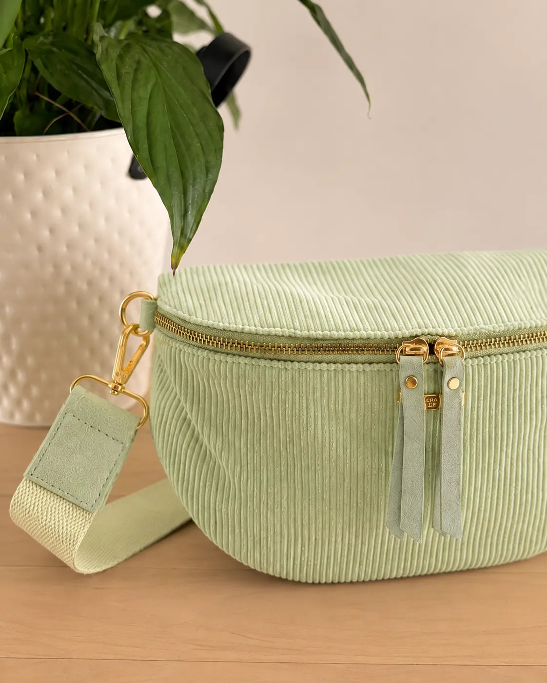 Sac banane velours côtelé vert menthe posée sur une table avec trousseau et plante en pot.