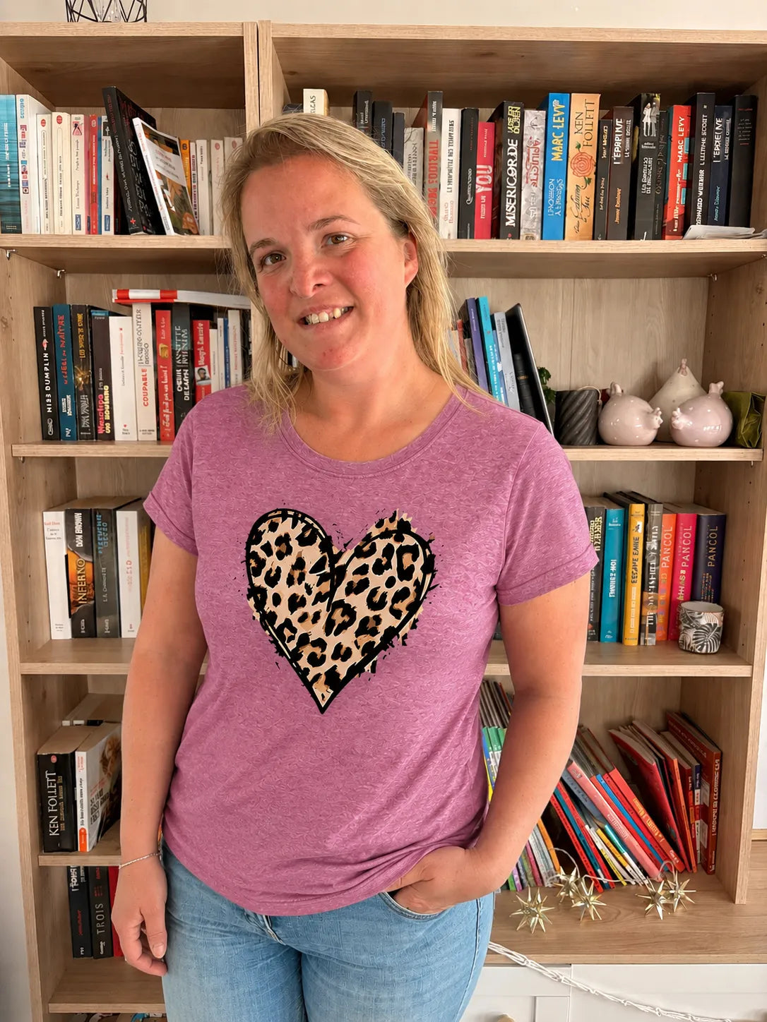 T-shirt rose casual chic avec cœur imprimé léopard, porté par une femme devant une bibliothèque.