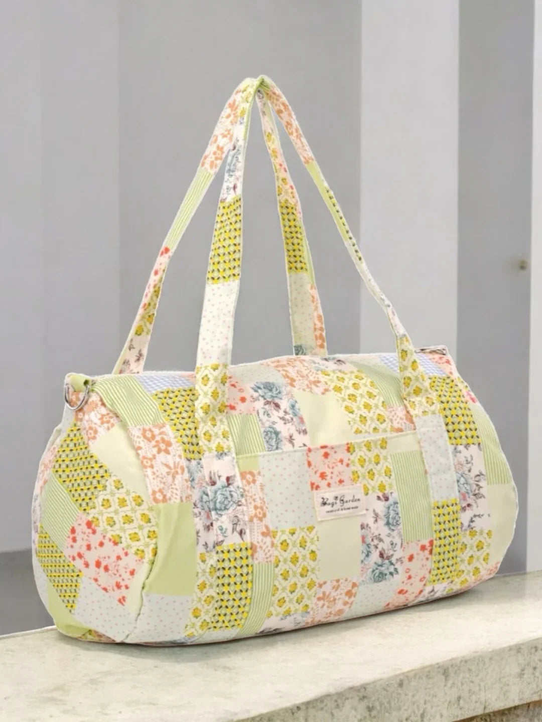 Sac polochon patchwork multicolore en tissu coton fleuri vert et jaune, posé sur un rebord en marbre
