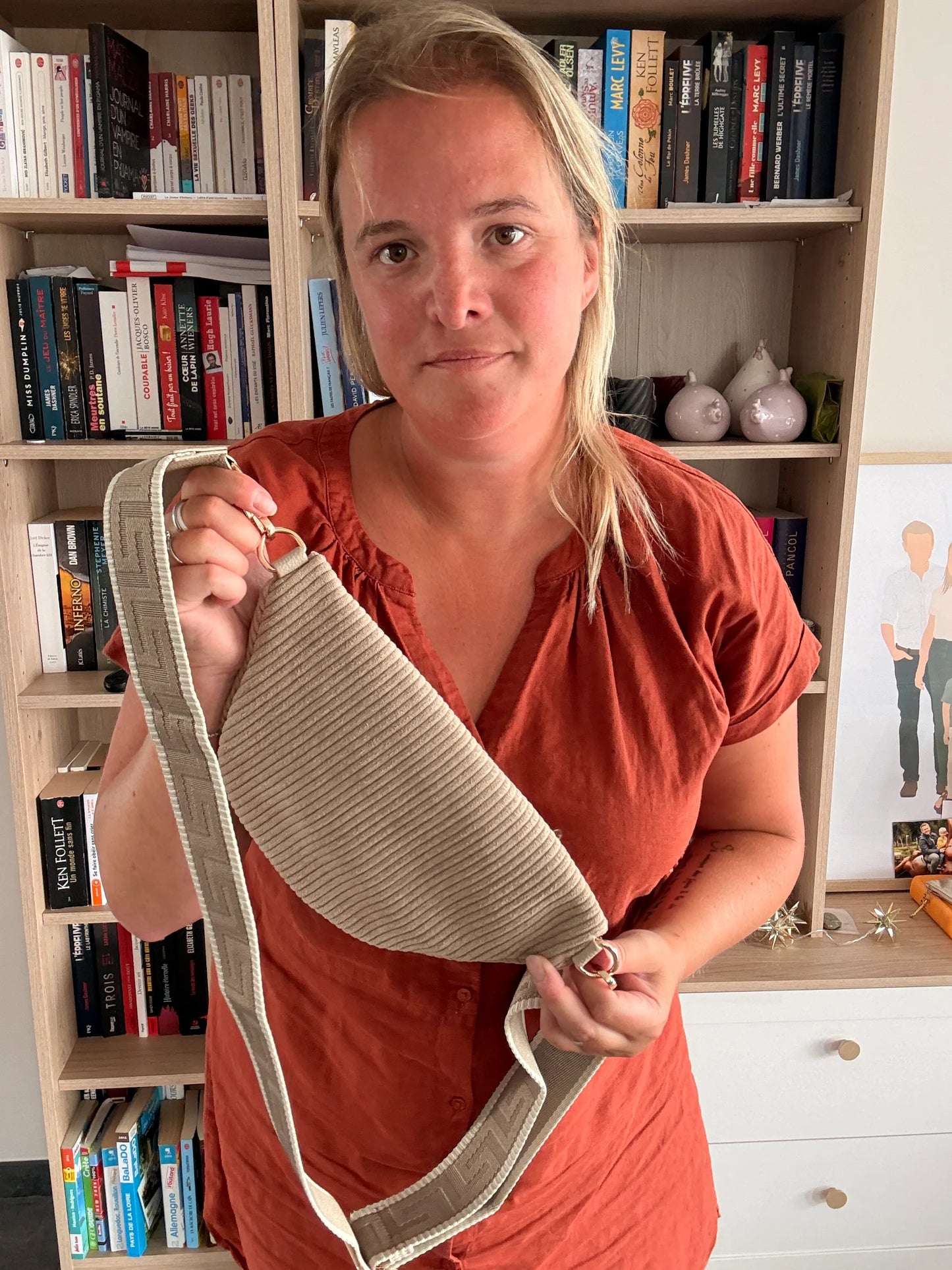 Sac banane Velours côtelé taupe avec sangle dorée, montrée par une femme tenant l’accessoire près du corps.