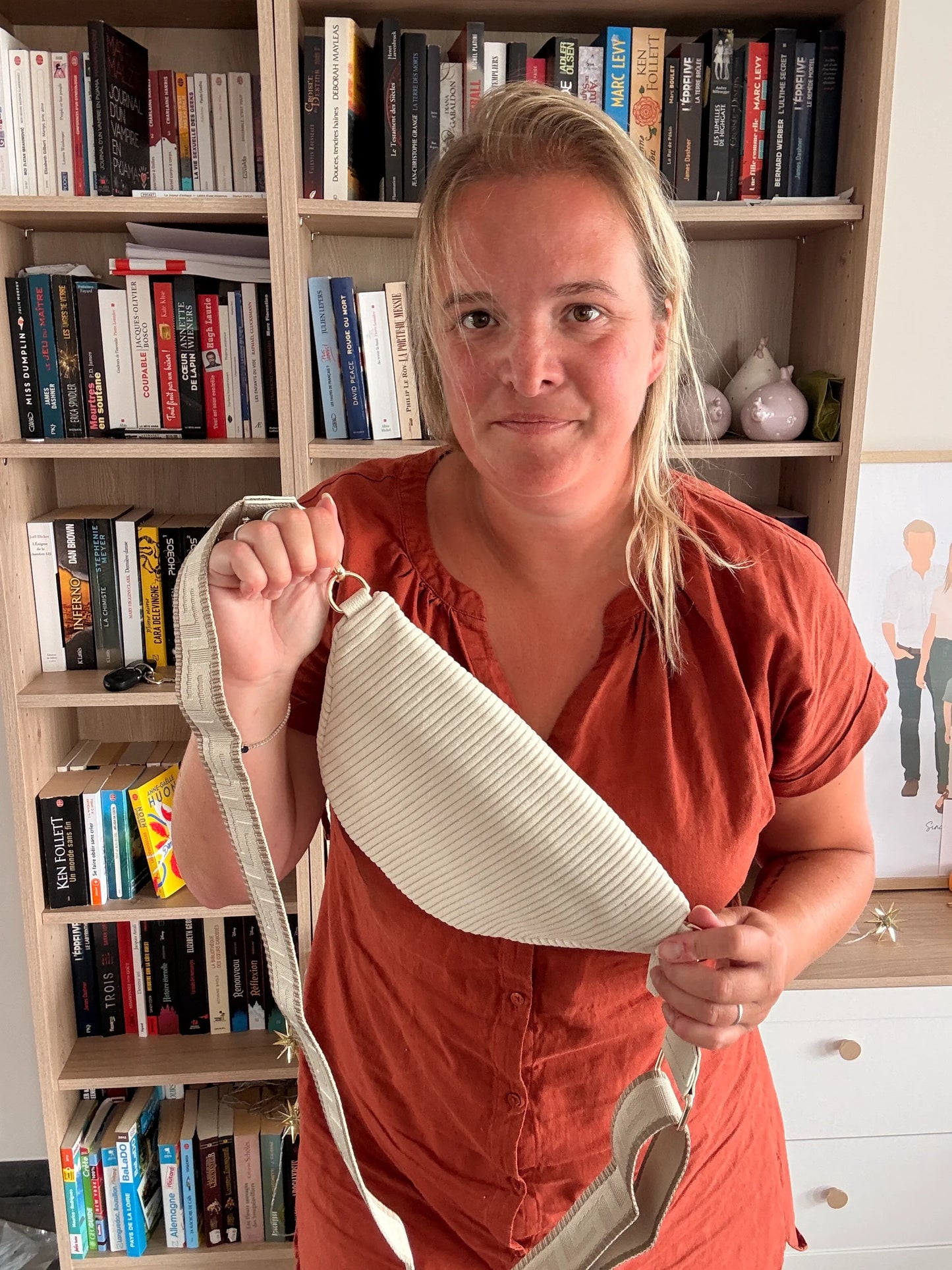 Sac Banane Velours Côtelé Beige affiché par une femme tenant la sangle avec zips dorés, devant une bibliothèque.