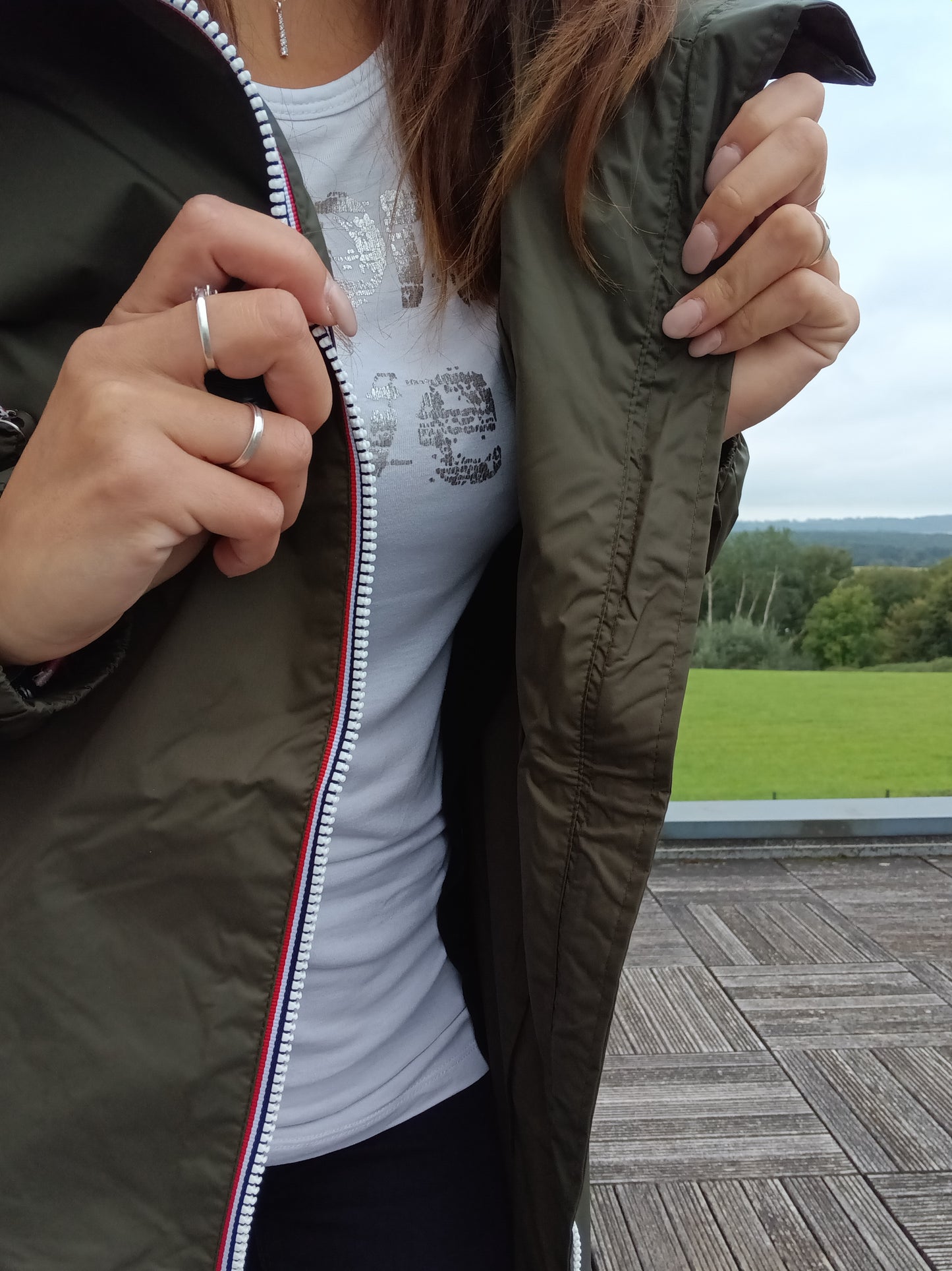 Woman wearing khaki Laura Jo raincoat outdoors, opening jacket to show white t-shirt