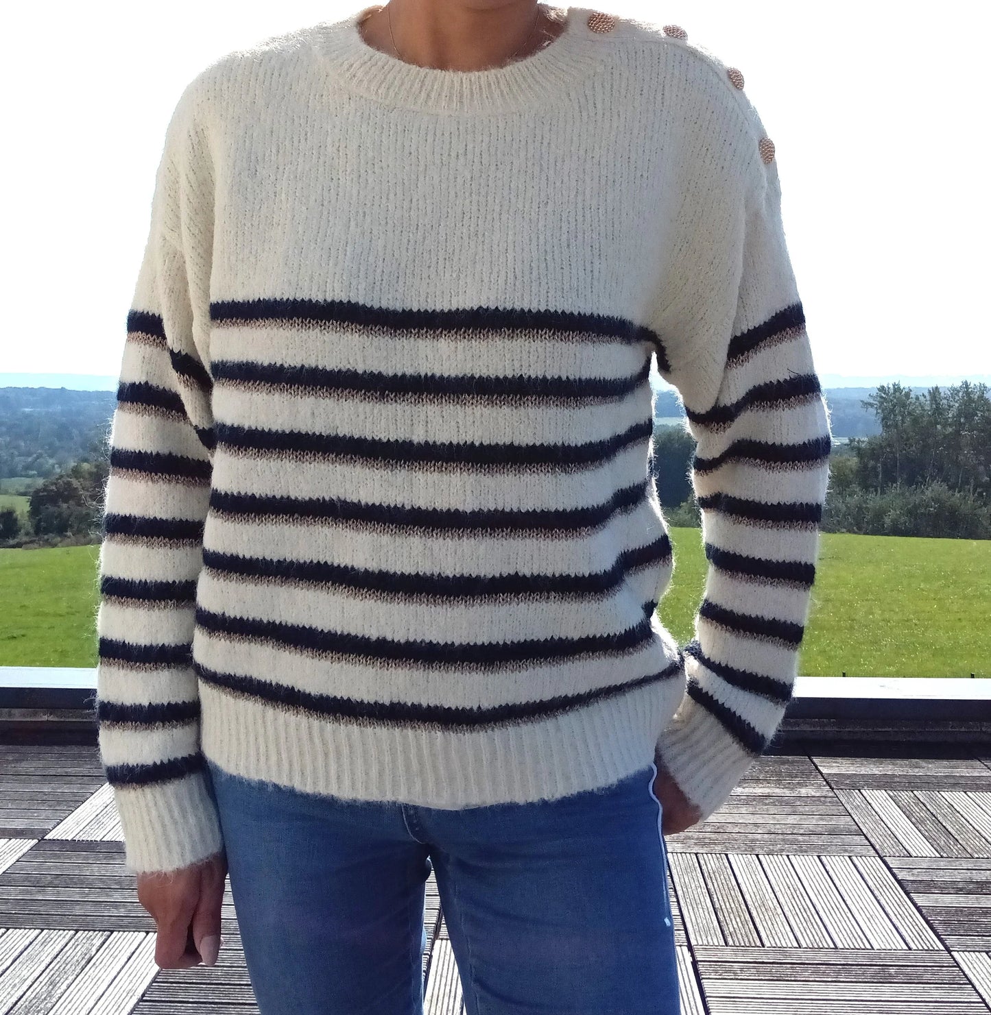 Pull fond blanc double rayures bleu marine et doré avec boutons dorés à l'encolure, porté avec un jean