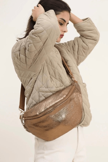 Woman wearing a beige quilted coat with a large metallic bronze belt bag from Le Petit Placard