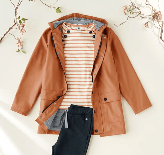 Rust raincoat with striped shirt and black pants flat lay, Le Petit Placard fashion style