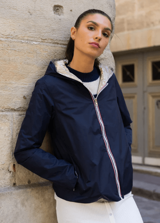 Woman in lightweight navy Laura Jo raincoat, leaning on stone wall in urban setting, Le Petit Placard