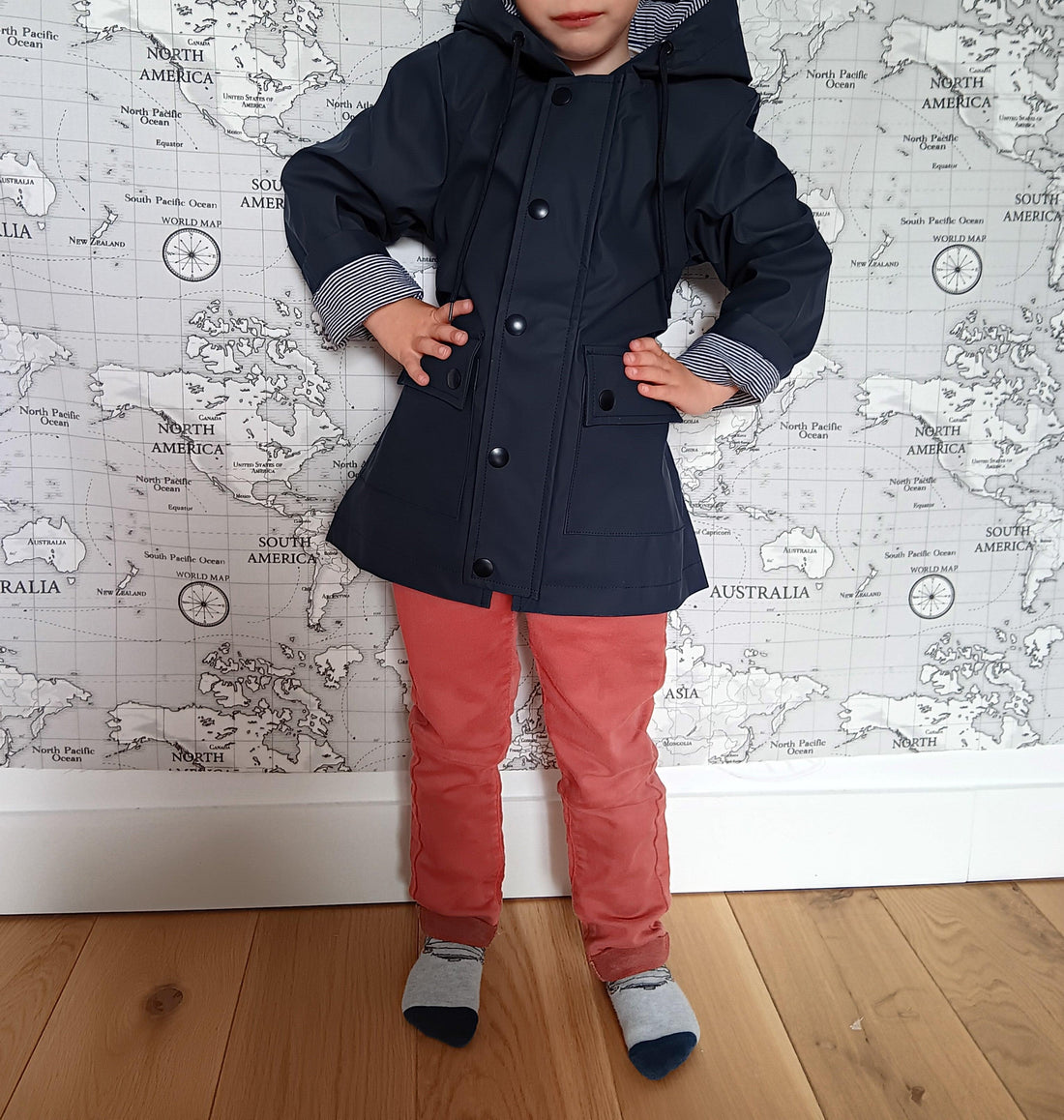 Child in navy raincoat and red pants, Le Petit Placard kids fashion, world map background