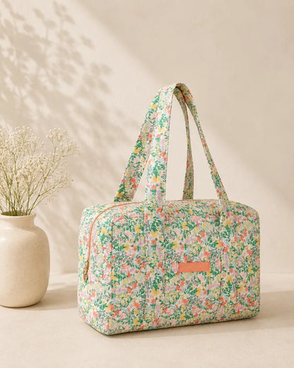 Sac polochon matelassé imprimé fleurs vert menthe, avec poignet(s) et fermeture zippée sur fond clair.