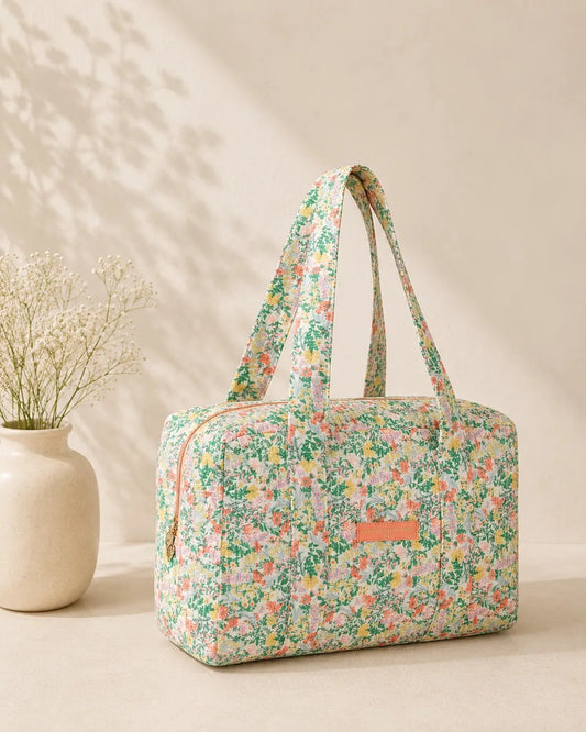 Sac polochon matelassé imprimé fleurs vert menthe, avec poignet(s) et fermeture zippée sur fond clair.