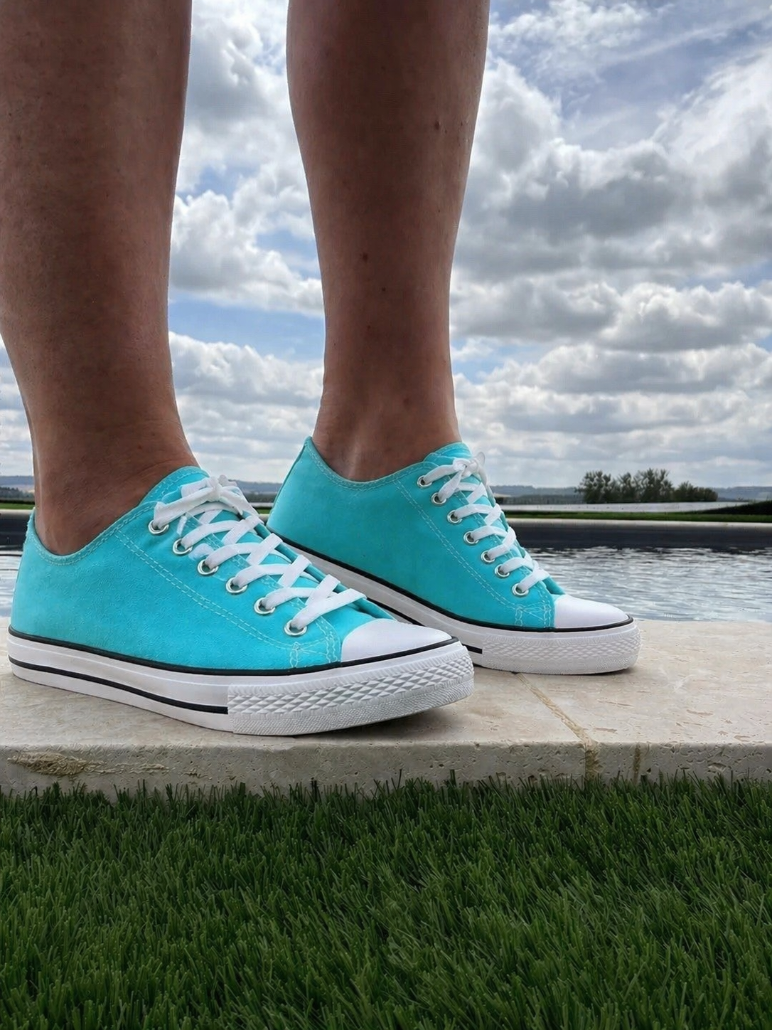Chaussures Converse turquoise à lacets, plateformes basses, vue de côté près d’un plan d’eau et d’un ciel nuageux.