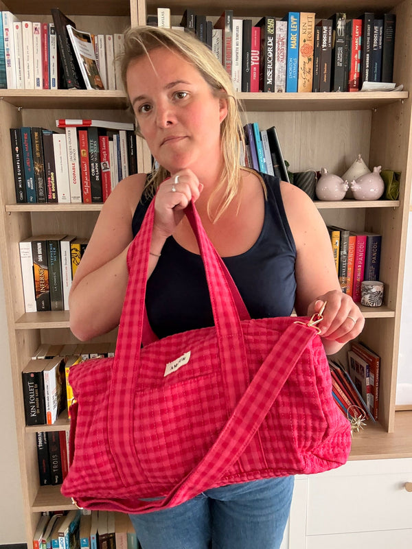 Sac polochon matelassé carré rouge porté par une femme en intérieur, près d’une étagère remplie de livres.