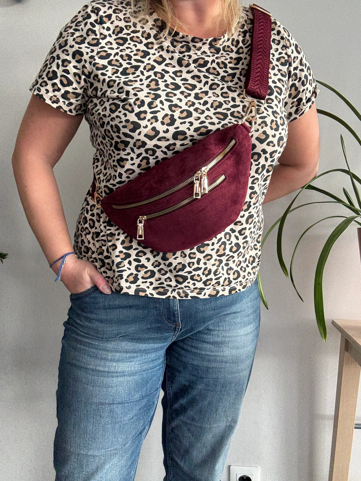 Sac banane toucher daim bordeaux à 2 poches zip doré porté en bandoulière sur tenue léopard et jean