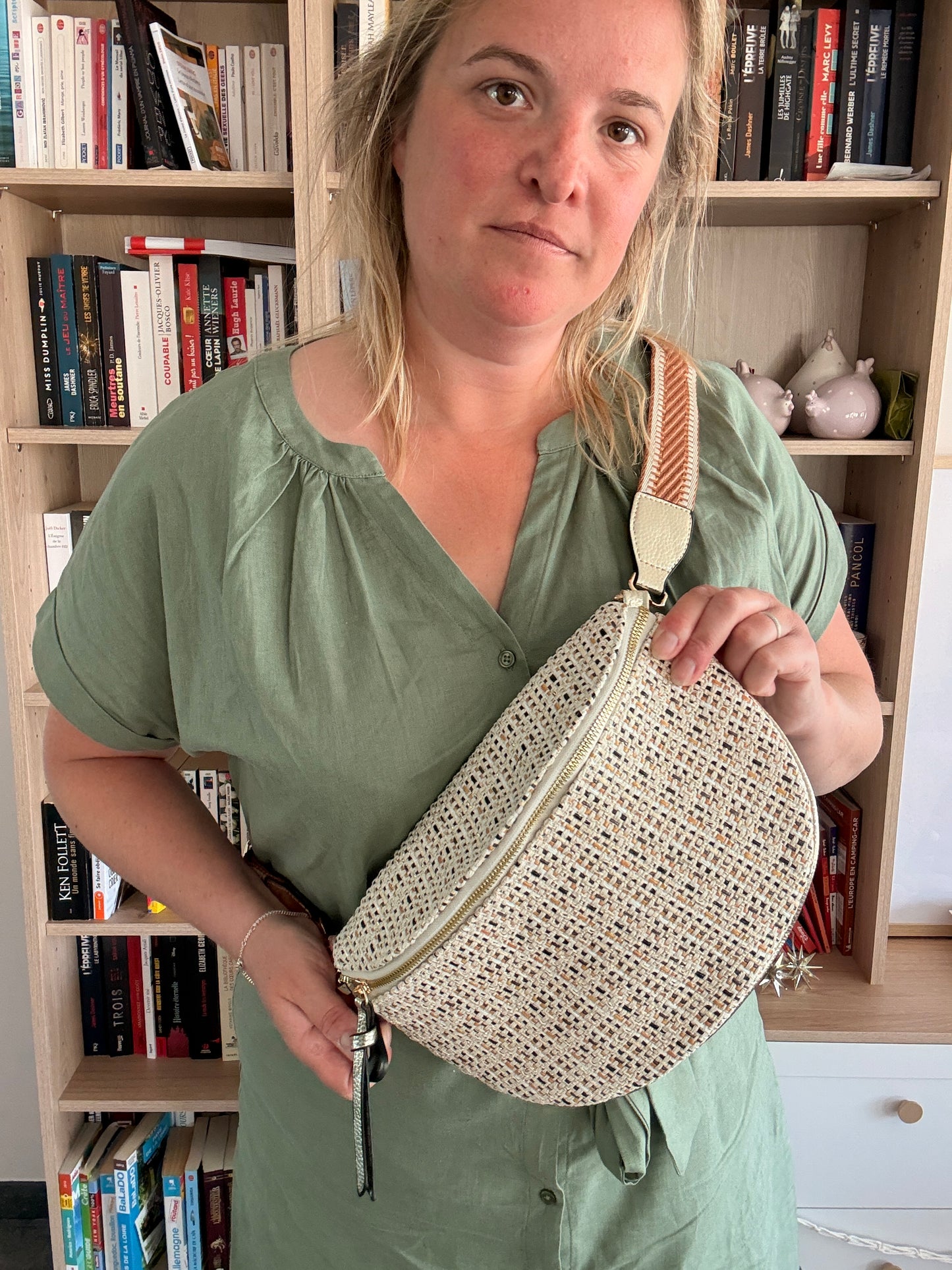 Sac banane en tissu motif bohème, porté en bandoulière par une femme devant une bibliothèque ; couleur beige et crème avec fines touches camel.