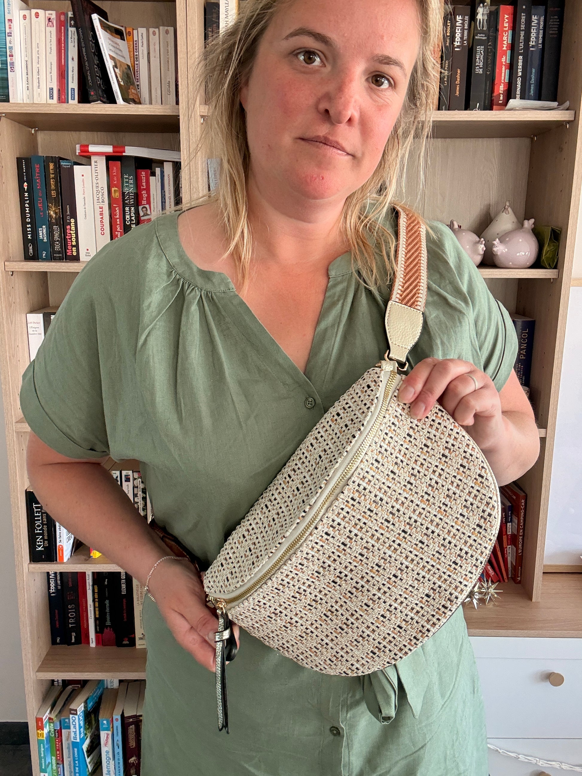 Sac banane en tissu motif bohème, porté en bandoulière par une femme devant une bibliothèque ; couleur beige et crème avec fines touches camel.