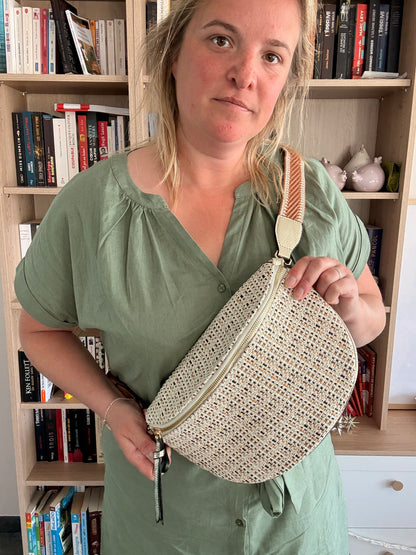 Sac banane en tissu motif bohème, porté en bandoulière par une femme devant une bibliothèque ; couleur beige et crème avec fines touches camel.