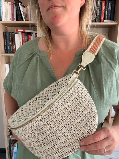 Sac banane en tissu motif bohème noir, beige et camel porté crossbody par une femme, fond bibliothèque.
