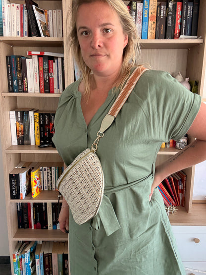 Sac banane tissée noir, beige et camel porté en bandoulière par une femme devant une bibliothèque.