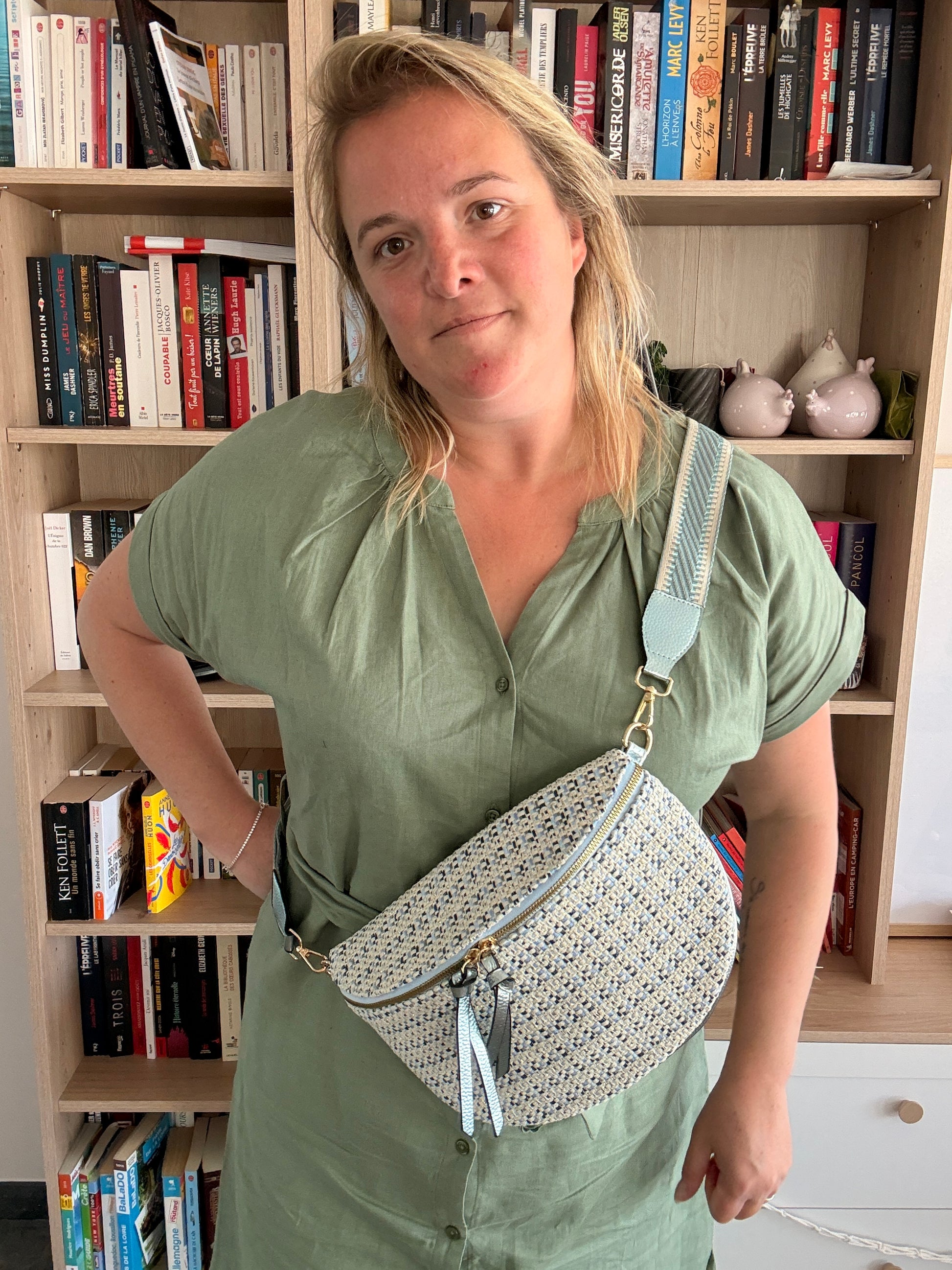 Sac banane en tissu à motif texturé couleur blanc cassé avec touches bleu clair, porté crossbody sur fond bibliothèque.