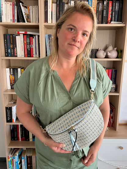 Sac banane en tissu à motif texturé noir, bleu et beige porté en diagonal, avec sangle fantaisie et fermeture zippée.