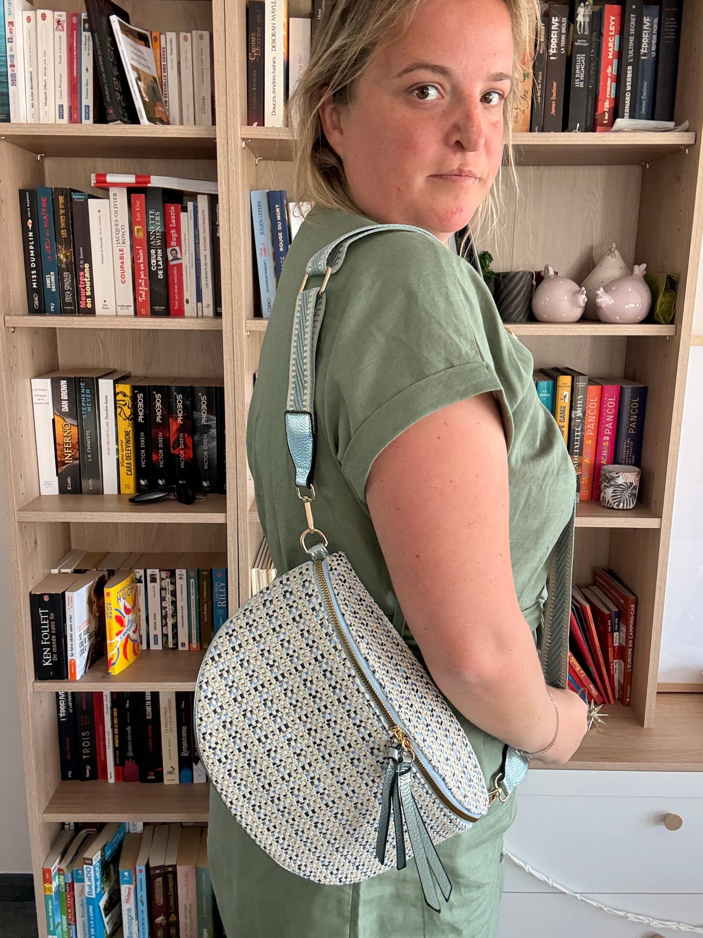 Sac banane en tissu texturé affichant motifs beige, bleu et noir porté en bandoulière par une femme dans une bibliothèque.