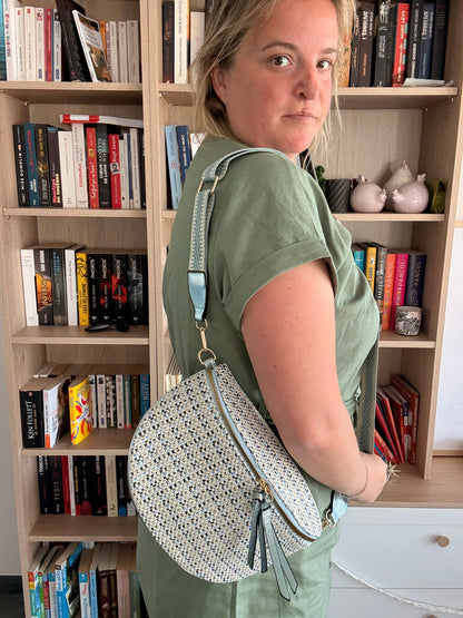 Sac banane en tissu texturé affichant motifs beige, bleu et noir porté en bandoulière par une femme dans une bibliothèque.
