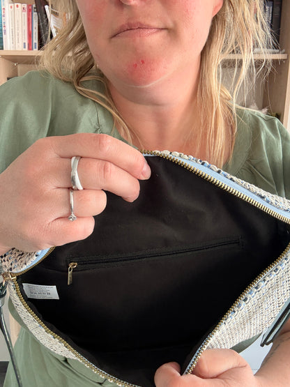 Sac banane en tissu ouvert pour montrer l’intérieur, avec poche zippée noire et doublure noire. Motif texturé sur l’extérieur et chaîne / sangle fantaisie visible.