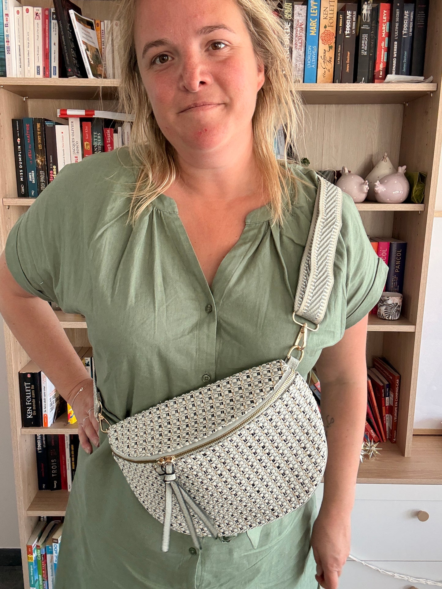 Sac banane en tissu texturé motif crochet blanc et noir, porté en bandeau sur l’épaule avec une lanière bleutée, posé sur le torse d’une femme.