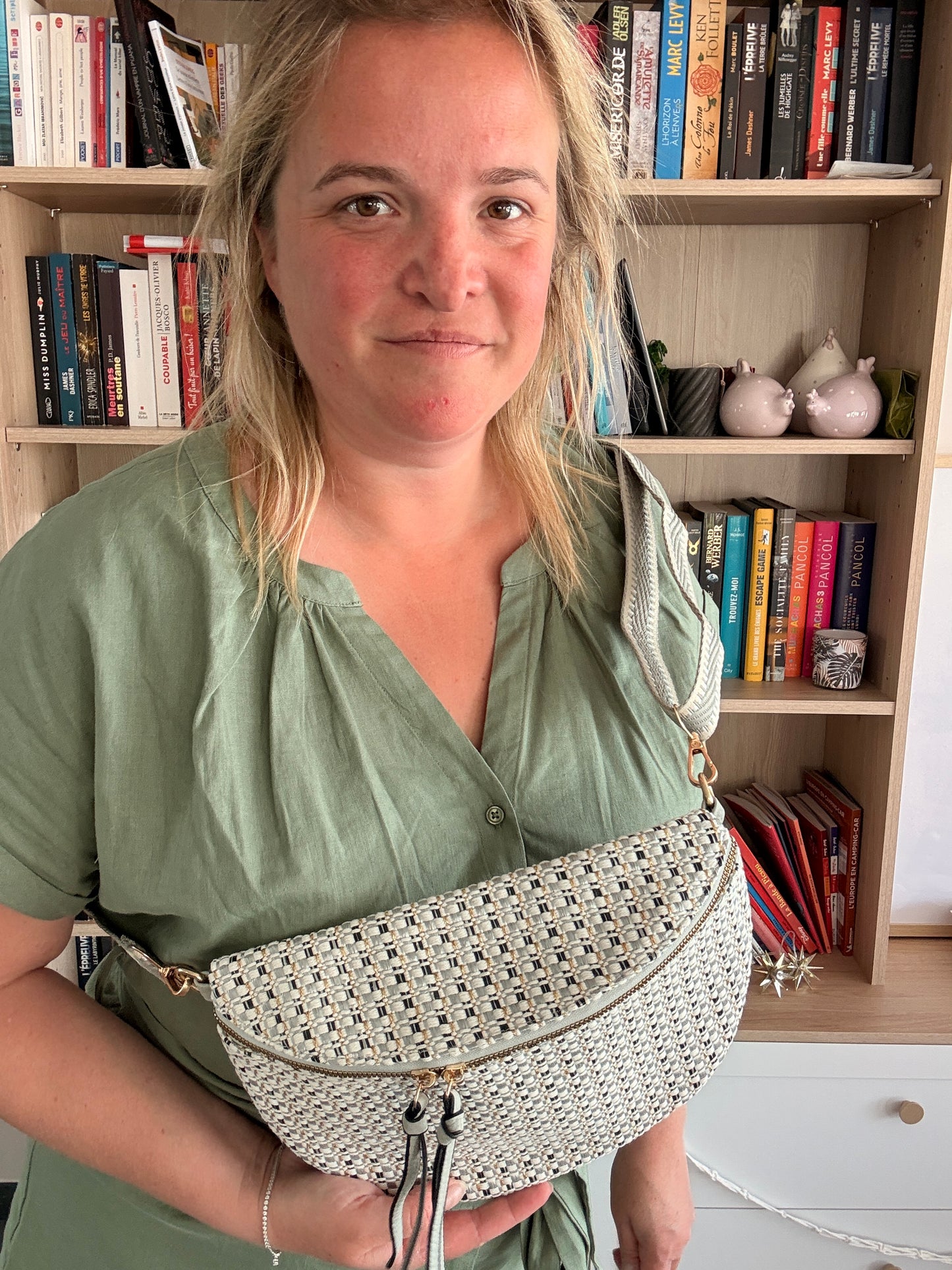 Sac Banane Tissu Texturé montrant une femme tenant une sacoche blanche à motif géométrique, avec une bibliothèque en arrière-plan.