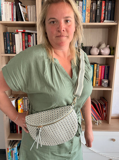 Sac banane en tissu texturé avec motif clair, portée en bandoulière par une femme devant une étagère de livres.