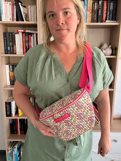 Sac banane Liberty fleuri rose porté en bandoulière, avec coton beige et finitions dorées visibles sur le zip et le détail.
