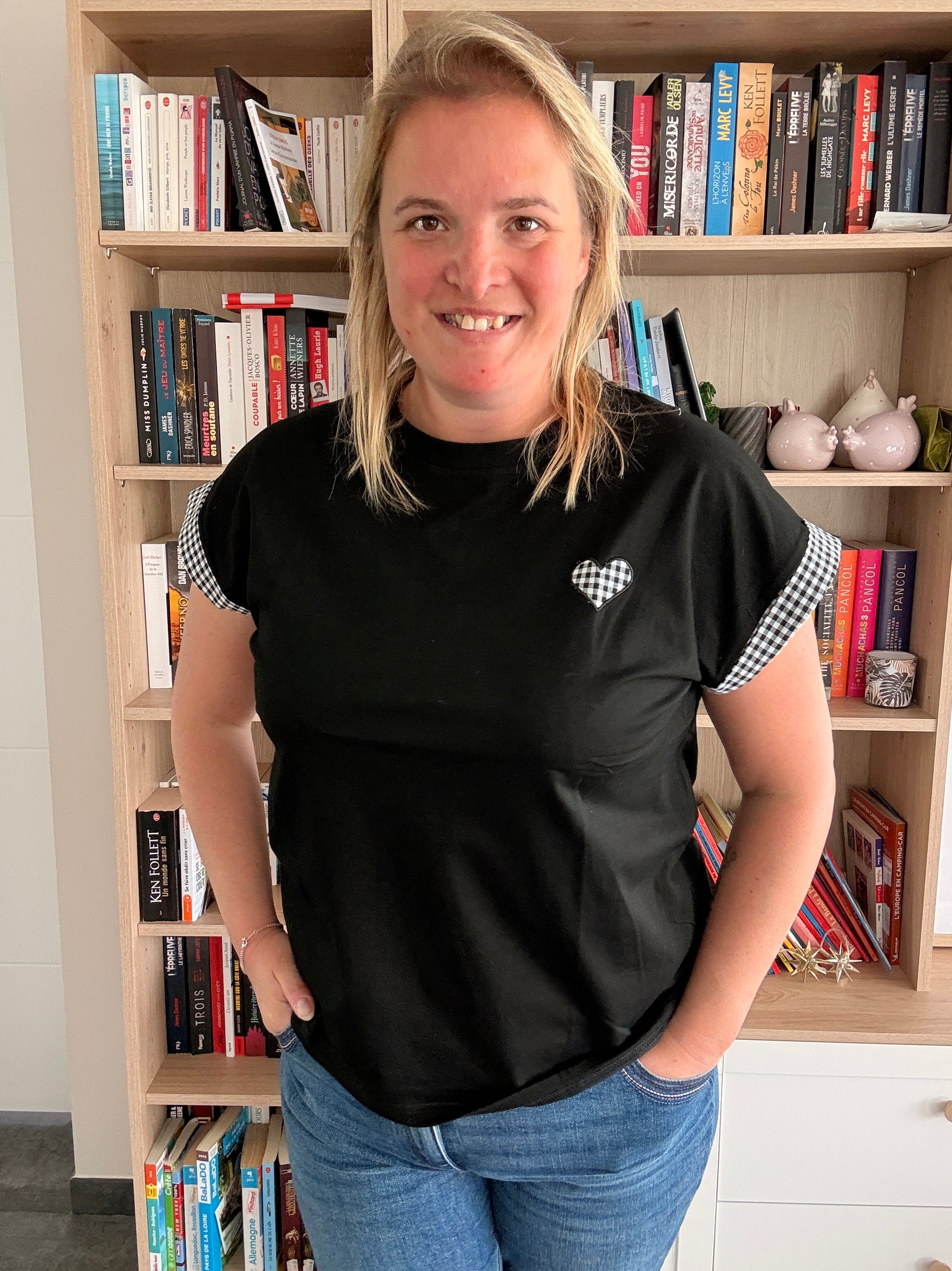 T-shirt femme noir oversize avec détails vichy noir et blanc, porté par une femme devant une étagère de livres.