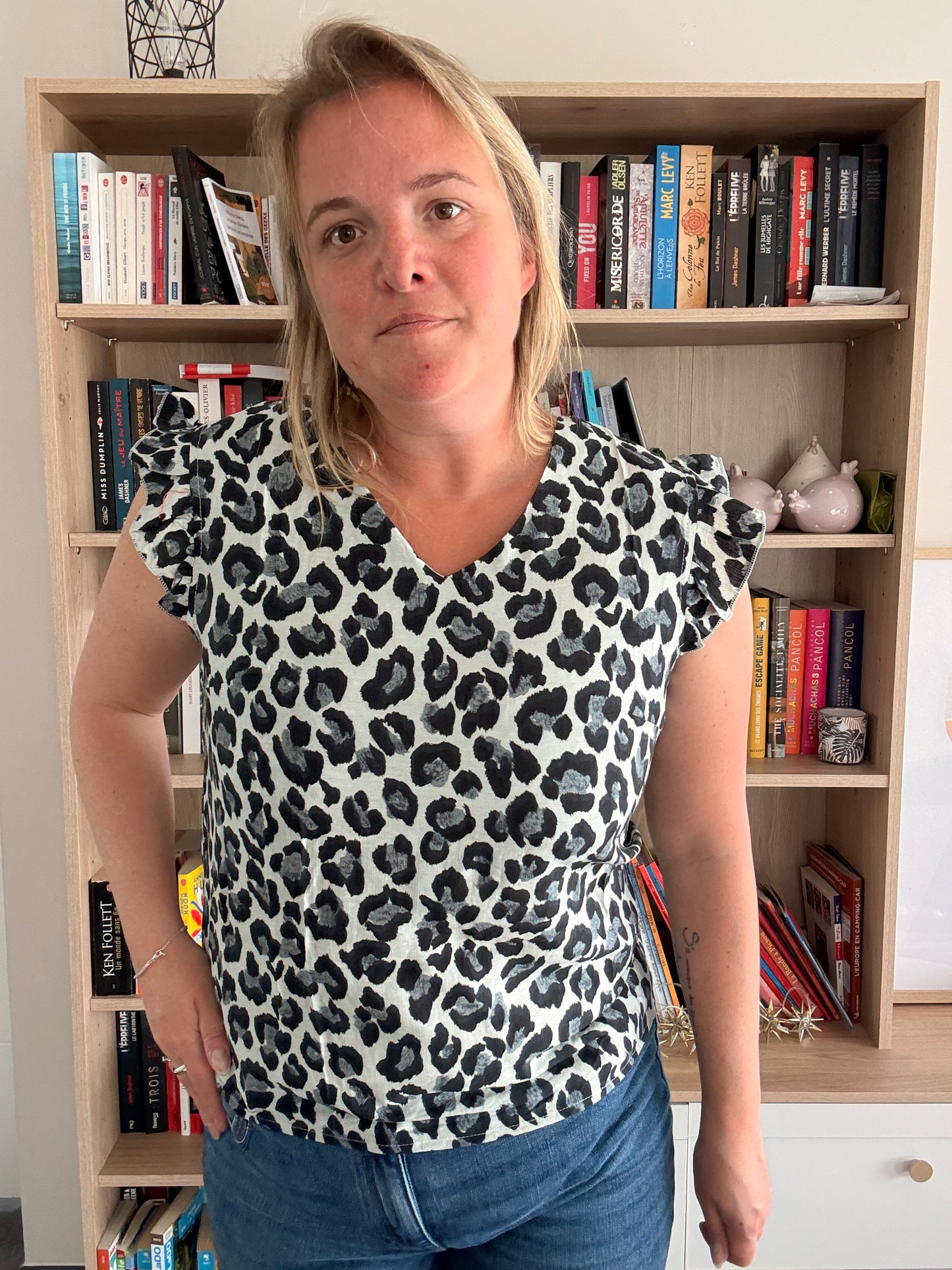 T-shirt col V pour femme sans manches léopard à volants noir et gris porté par une femme devant une bibliothèque.