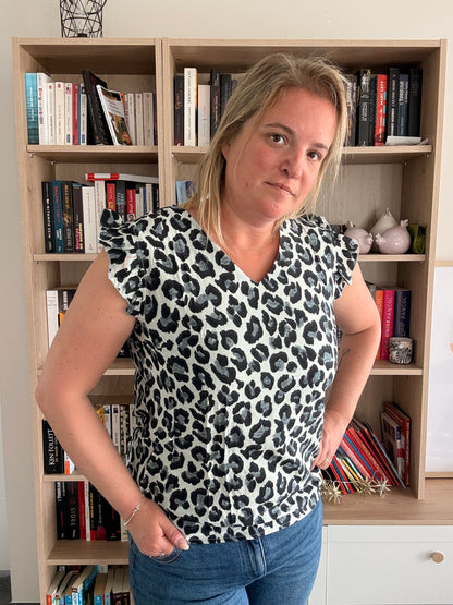 T-shirt femme sans manches à volants léopard noir et gris, porté par une femme debout dans une pièce avec bibliothèque.