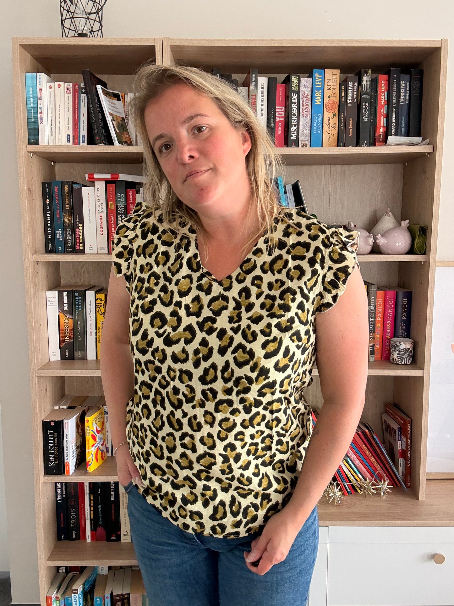 T-shirt col V femme sans manches léopard à volants couleur kaki porté par une femme, devant une bibliothèque.
