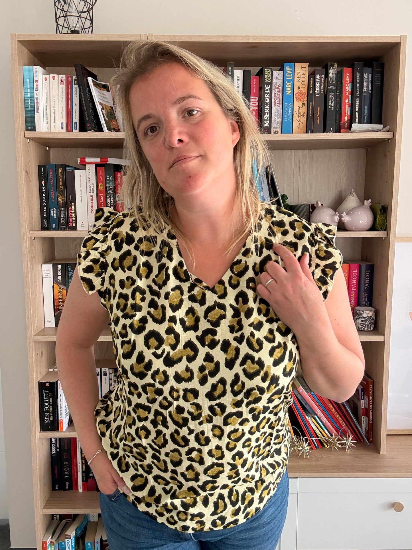 T-shirt col V femme sans manches à léopard avec volants, couleur kaki-vert porté par une femme devant une librairie.