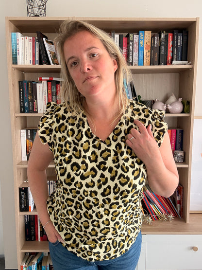 T-shirt col V femme sans manches à léopard avec volants, couleur kaki-vert porté par une femme devant une librairie.