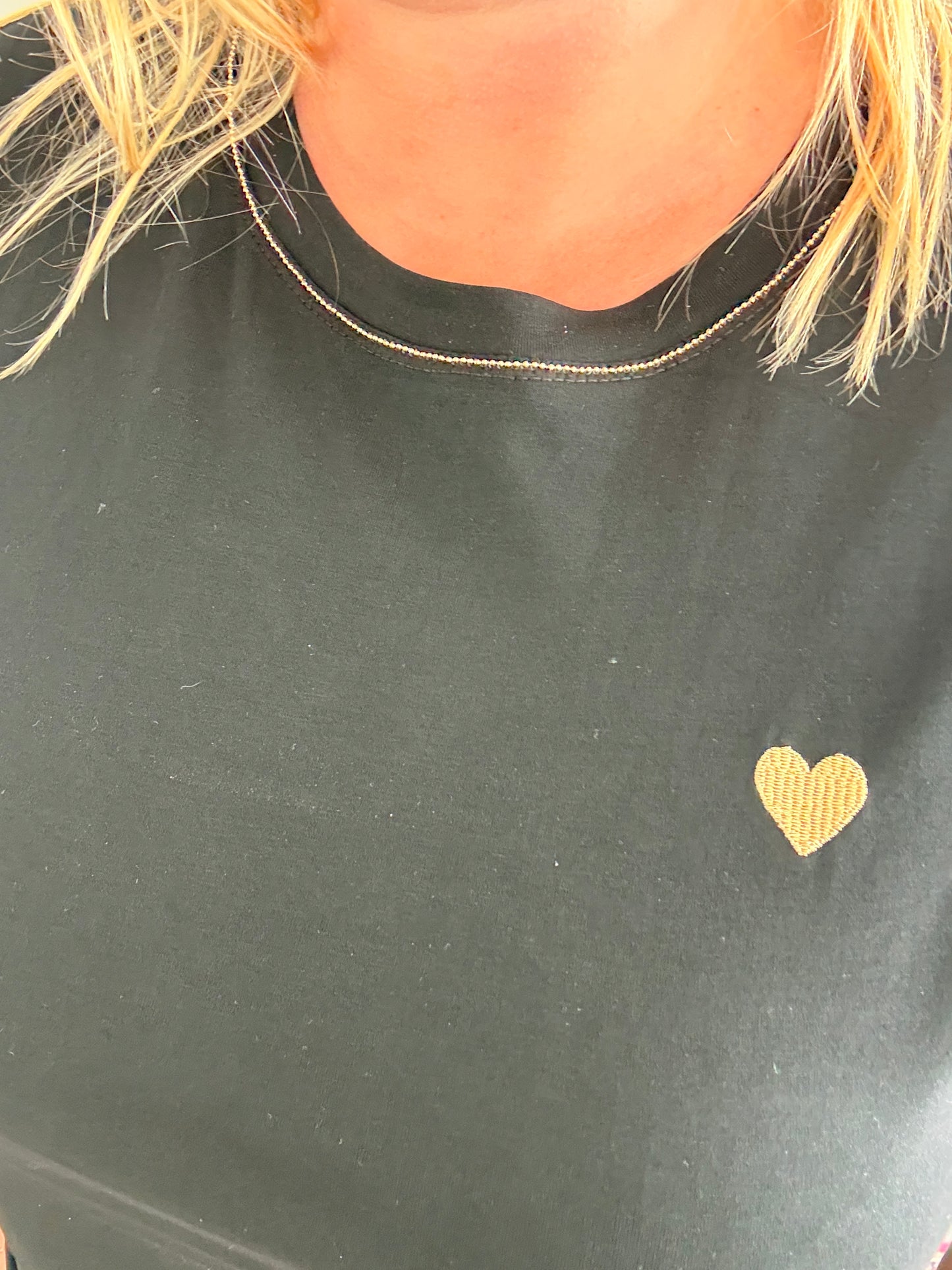 T-shirt noir avec petit cœur doré sur la poitrine et col rond.