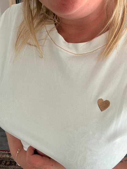 T-shirt blanc avec petit cœur doré sur la poitrine, col rond et détail brillant, femme portant premier plan.