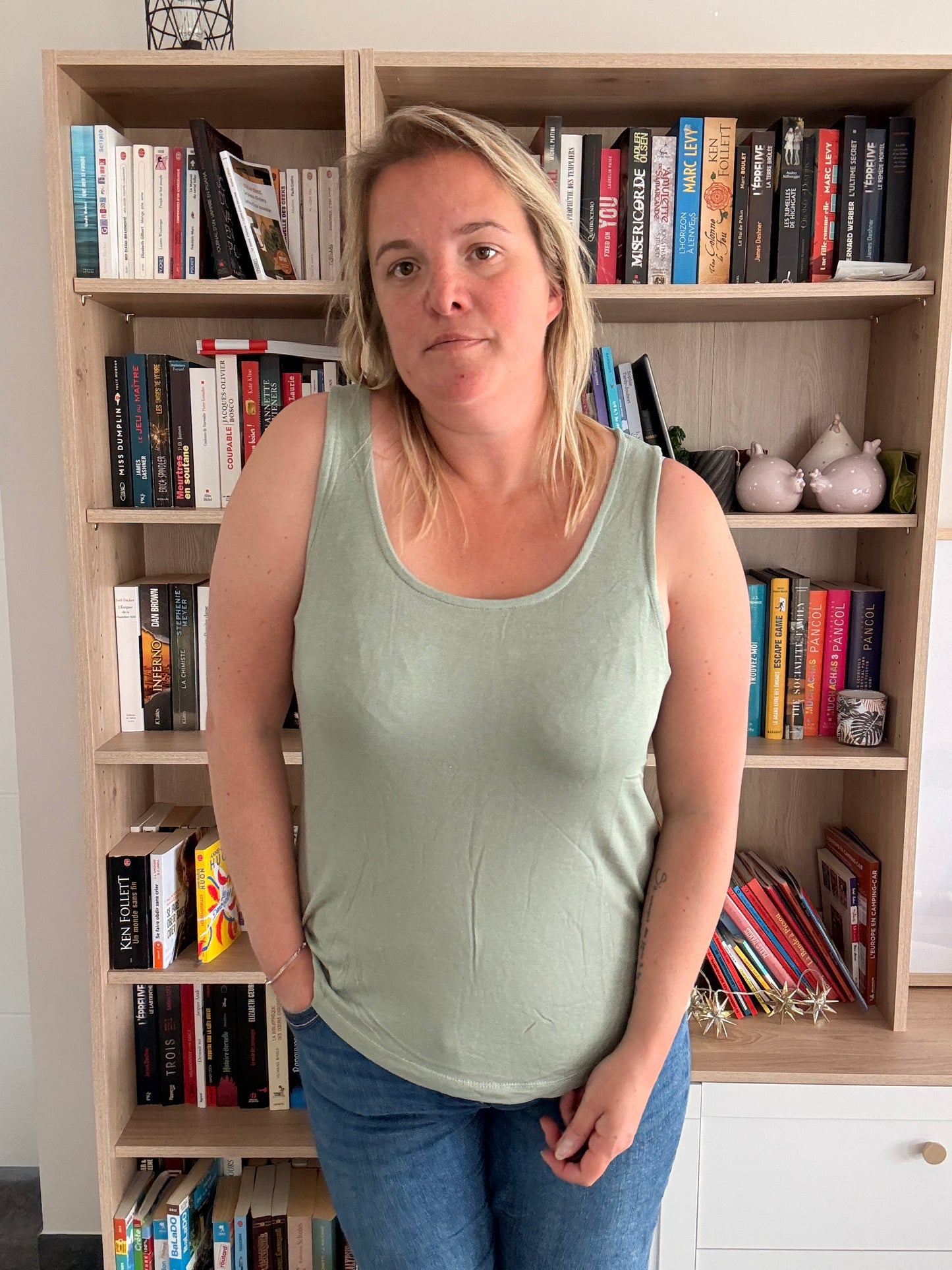 Débardeur coton lin kaki, coupe ample et légère, portée par une femme devant une étagère remplie de livres.