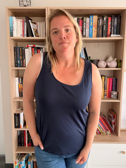Portrait d’une femme portant un débardeur bleu marine uni, debout près d'une bibliothèque remplie de livres.