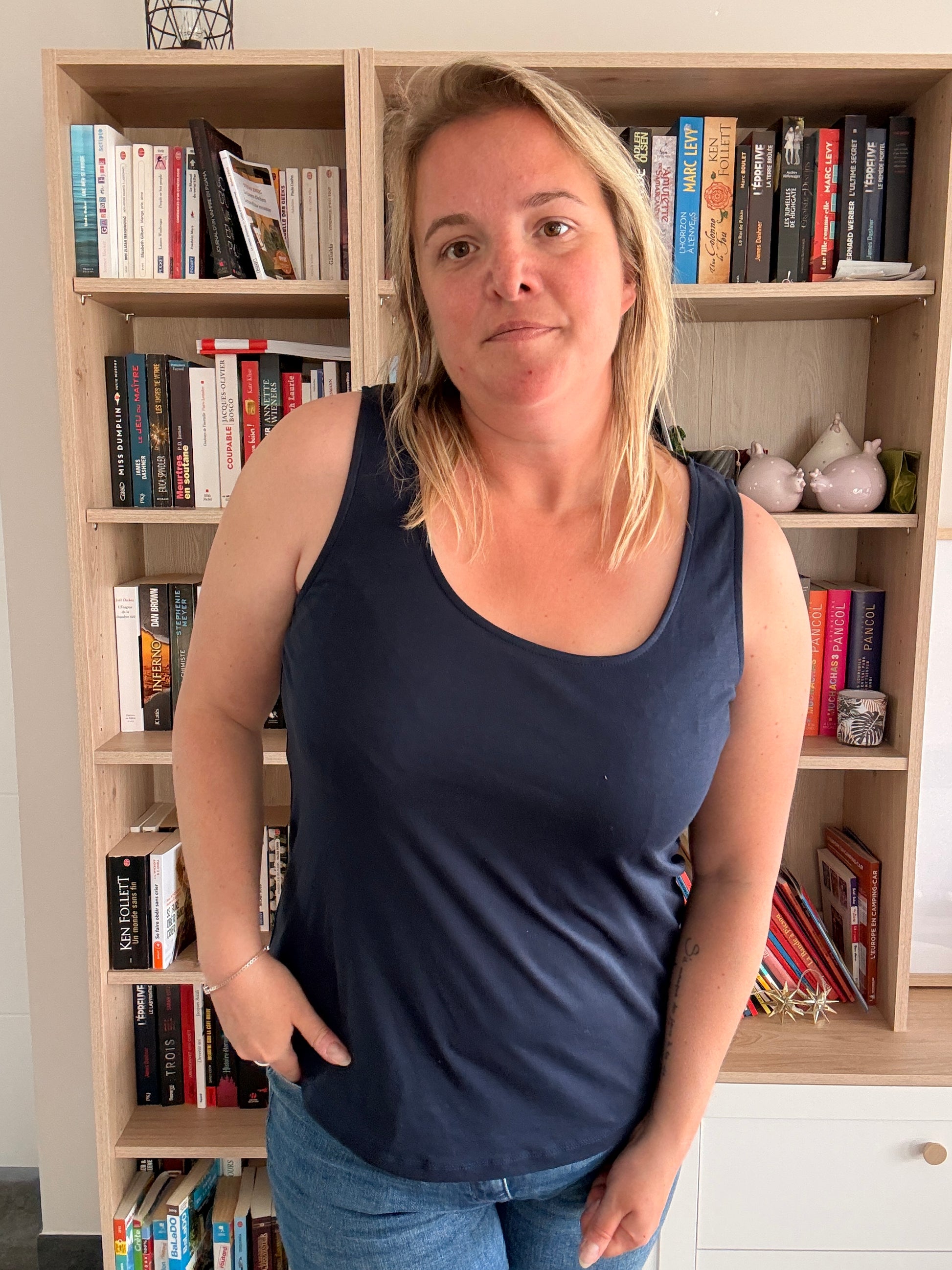 Femme portant un débardeur bleu marine uni et confortable, debout devant une étagère remplie de livres.