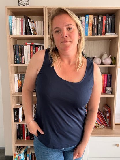 Femme portant un débardeur bleu marine uni et confortable, debout devant une étagère remplie de livres.