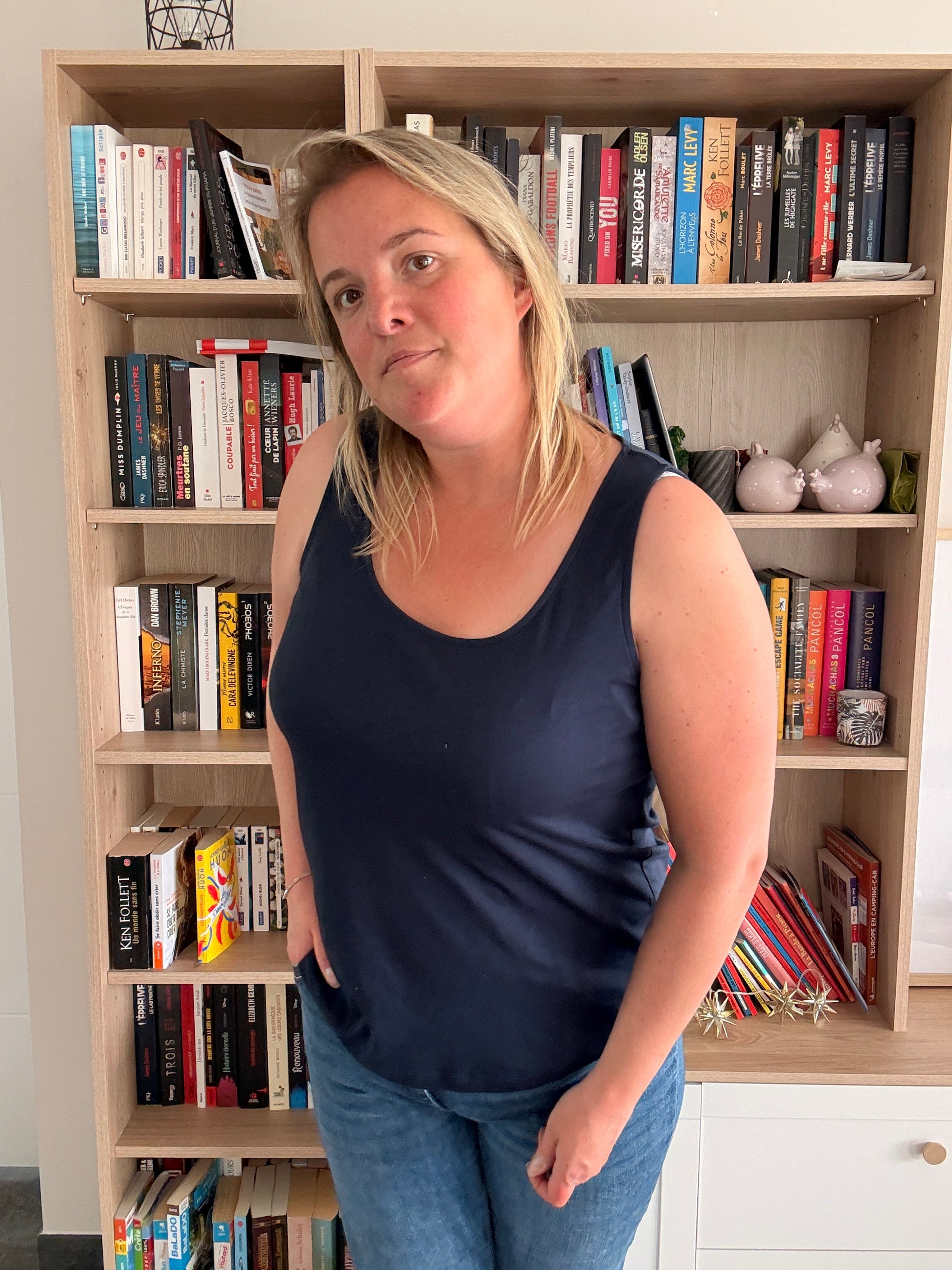 Femme portant un débardeur bleu marine uni et confortable, debout dans une bibliothèque remplie de livres.